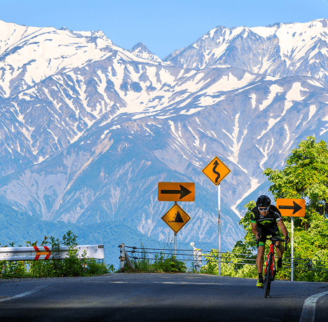 Cyclist riding with Nagano's mountains behind, the snow capped Japanese Alps.